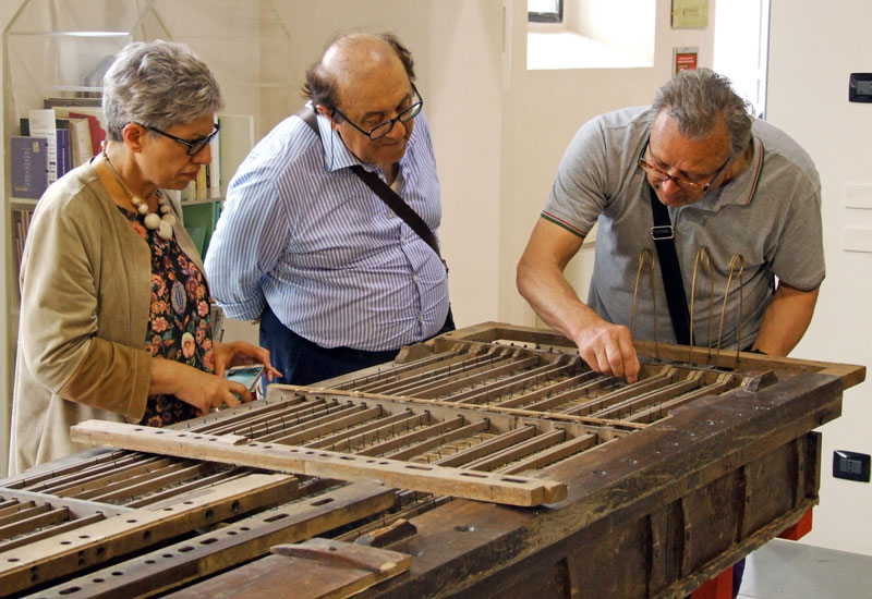 Il direttore del museo di organaria di Crema Sig. Sebastiano Guerini spiega con entusiasmo il funzionamento di un antico somiere a vento; il prof. Marchetti e la Sig.ra Spezzaferri seguono interessati.