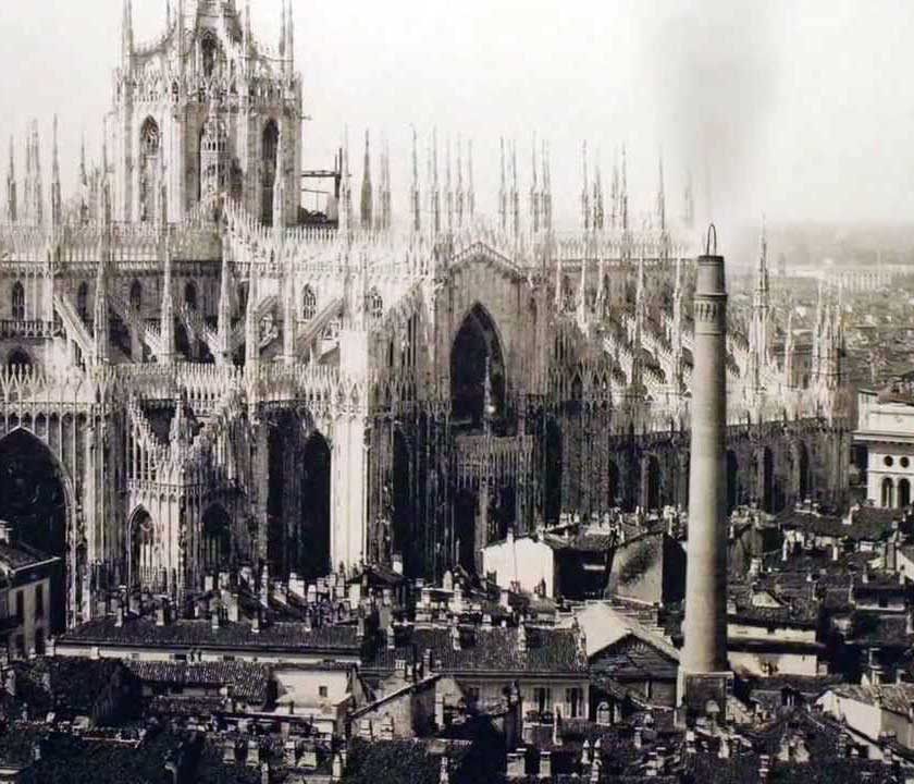 Fotografia che riprende la ciminiera fumante della centrale di Santa Radegonda; sullo sfondo l’imponente struttura del Duomo di Milano.